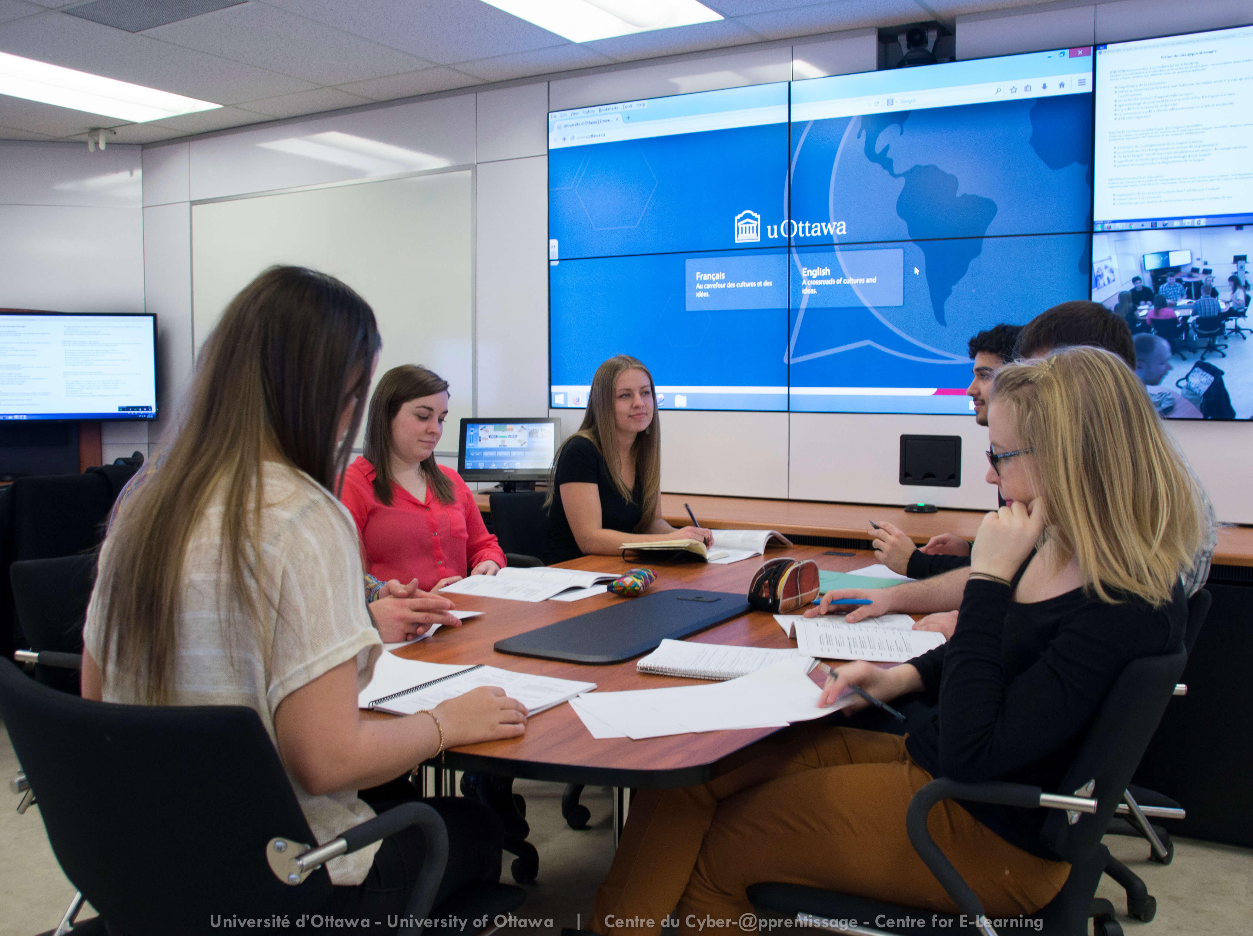 Photo salles de classe collaborative avec de grands écrans aux murs t des étudiantes et étudiants assis autour d'une table et