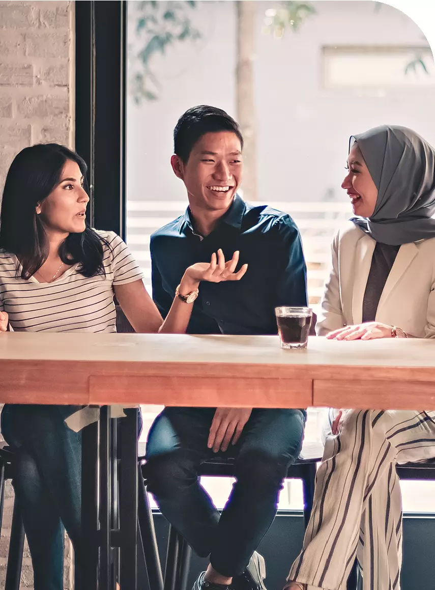 Trois personnes multiculturelles discutant à une table haute dans un café.