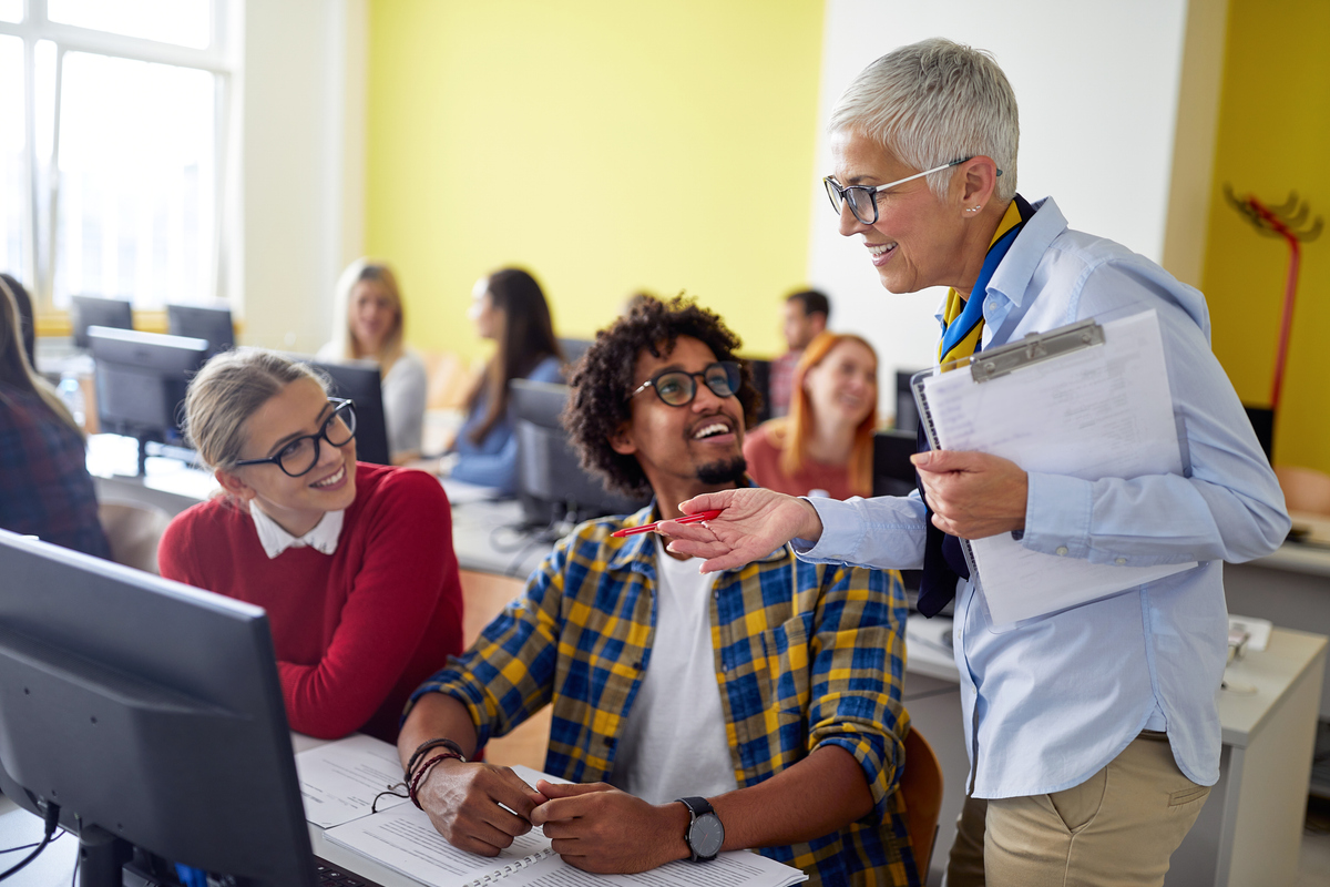 Une femme professeur évalue le travail des étudiants lors d'un cours d'informatique dans une salle de classe de l'université. Des jeunes gens intelligents étudient à l'université. Concept d'éducation, de collège, d'université, d'apprentissage et de personnes multiethniques.