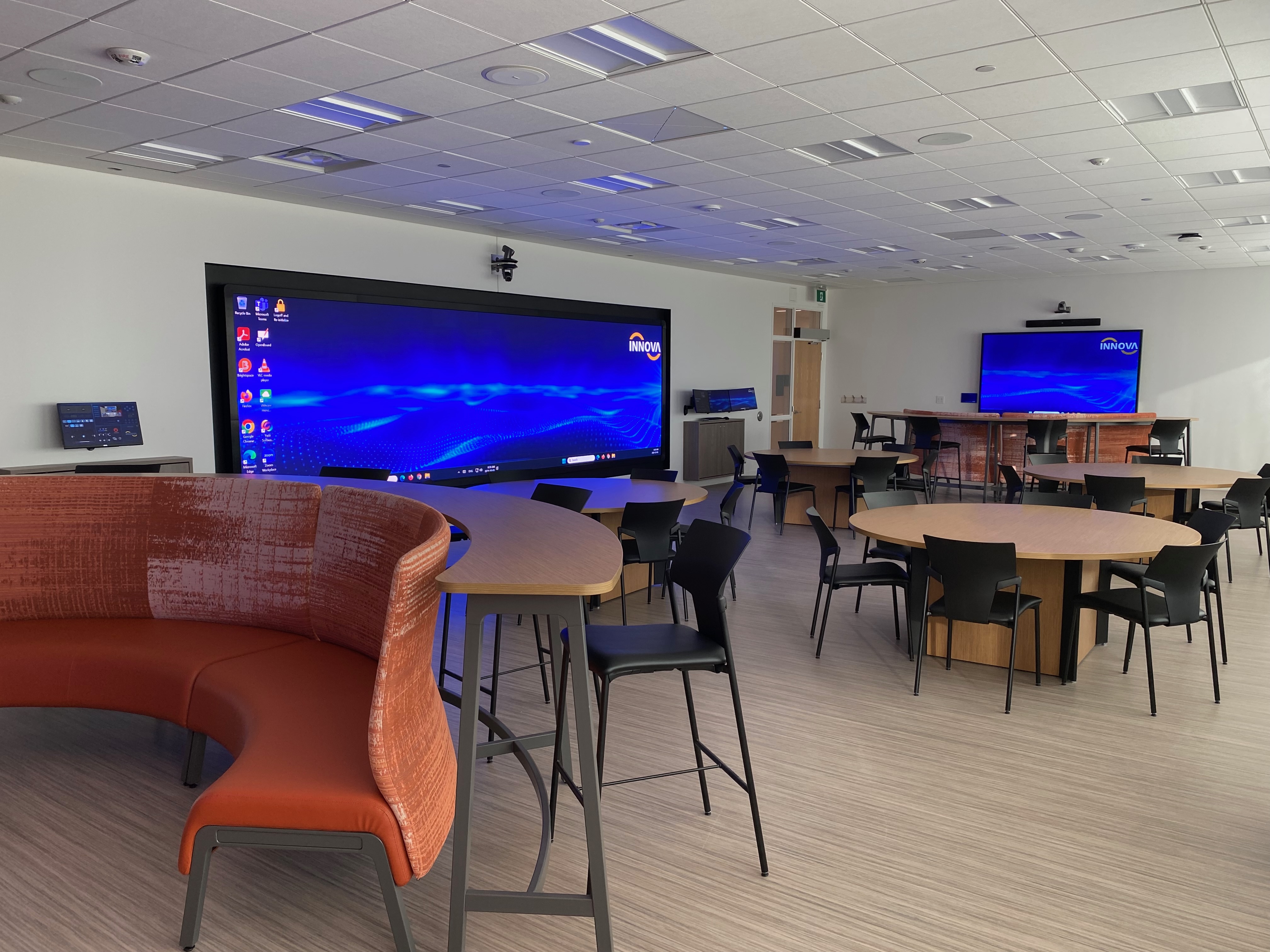 Photo of a collaborative classroom with large screens on the walls and students working.