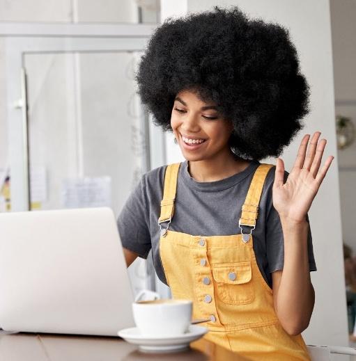 Smiling African woman using laptop video conference calling in cafe.